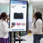 Two women chatting about a product displayed on a digital signage display screen inside a shopping store