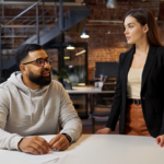 Two UK professionals, Omar and Jessica, engaged in a thoughtful conversation about AI adoption in a modern office setting.
