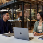 Zak and Sara in a UK office discussing product research strategies, both focused and engaged, with a real office background.