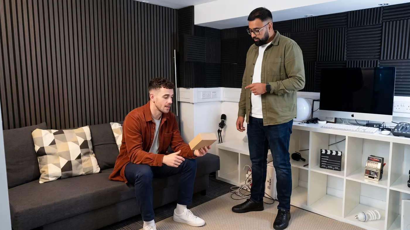 One colleague on a sofa shows a product sample to another in a small office.