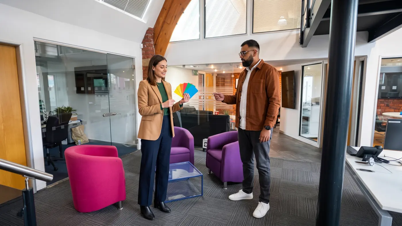 Two colleagues compare coloured content cards beside armchairs in a modern office lobby