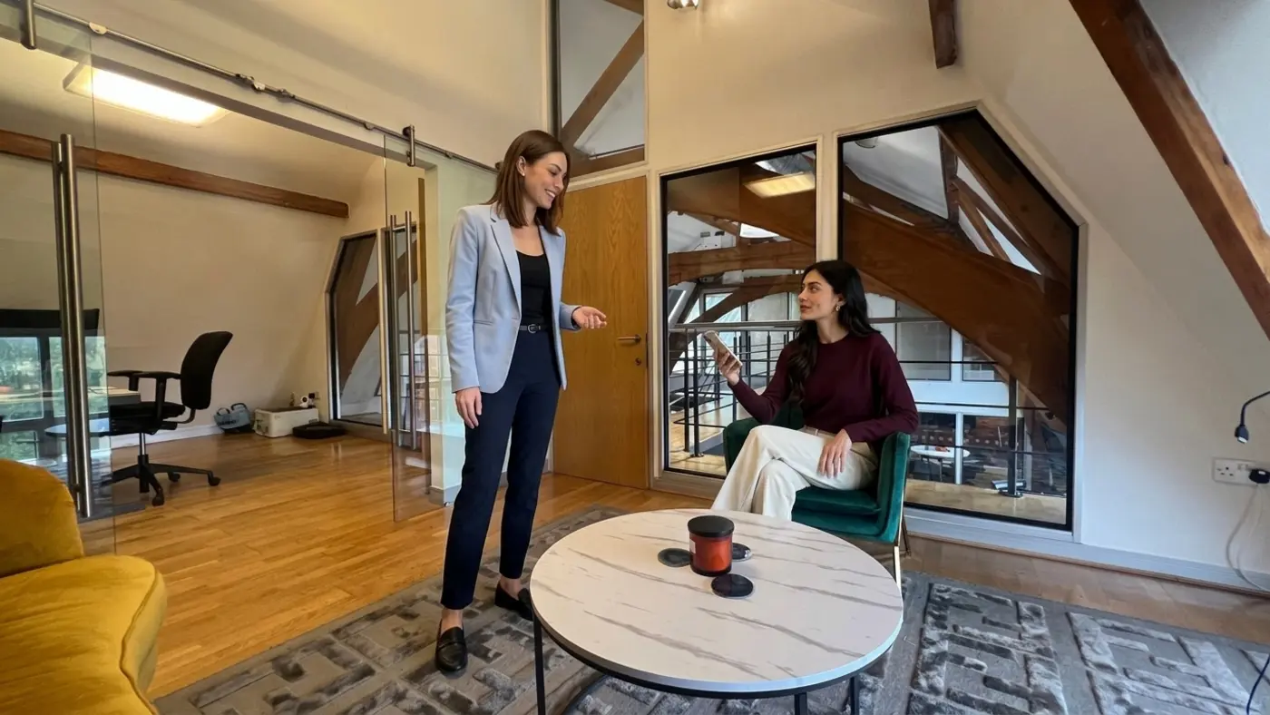 A seated colleague and standing colleague check a phone beside an office table
